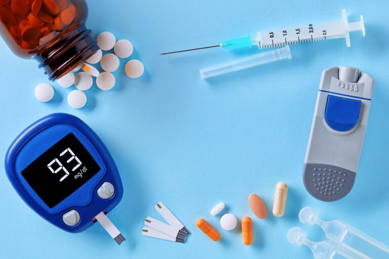 Diabetes monitoring and healthcare. Close up top down view of glucose meter, insulin pen, drug pills and syringe on blue background with copy space in the middle